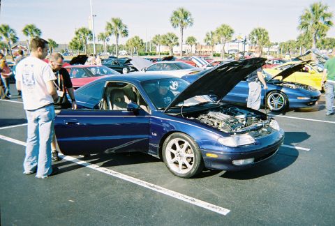 1991 Ford Probe - A dark blue coupe with its hood and driver's door open is parked in a lot with other cars.