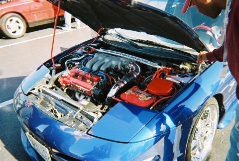 1991 Ford Probe - The engine bay of a blue car is open, revealing a V6 engine and custom modifications. A red car is parked nearby.