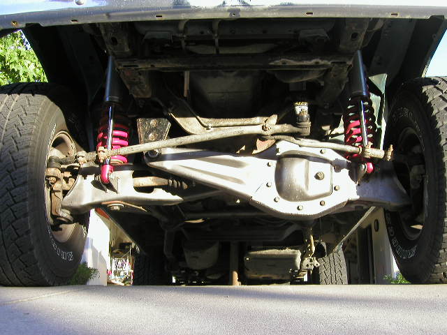 Underside view of a vehicle's suspension and drivetrain components, showing shocks, springs, and differential