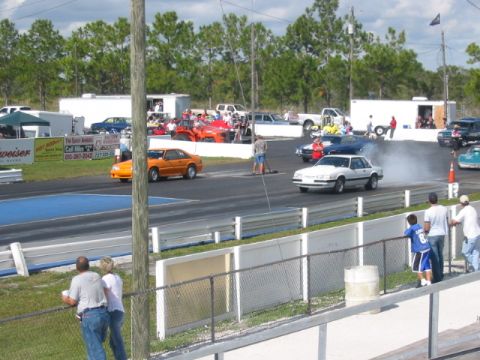 1997 Ford Crown Victoria - Cars compete on a drag strip with spectators in the background.
