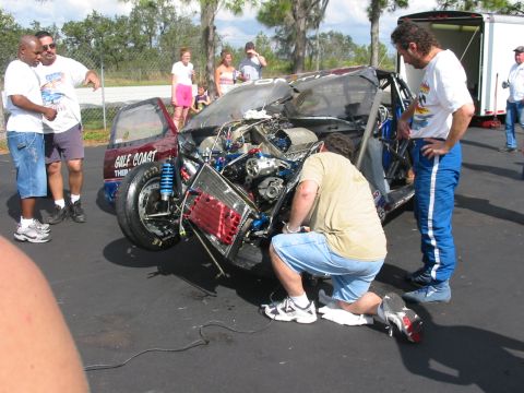 1997 Ford Crown Victoria - A severely damaged race car is examined by onlookers after an apparent accident, with its engine and front end heavily compromised.