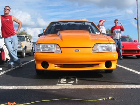 1997 Ford Crown Victoria - Modified orange Ford Mustang with racing decals on the windshield is parked at an outdoor event.