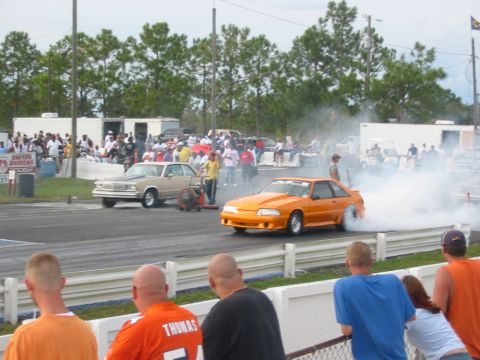 1997 Ford Crown Victoria - Two cars at a drag strip, one performing a burnout with thick smoke.