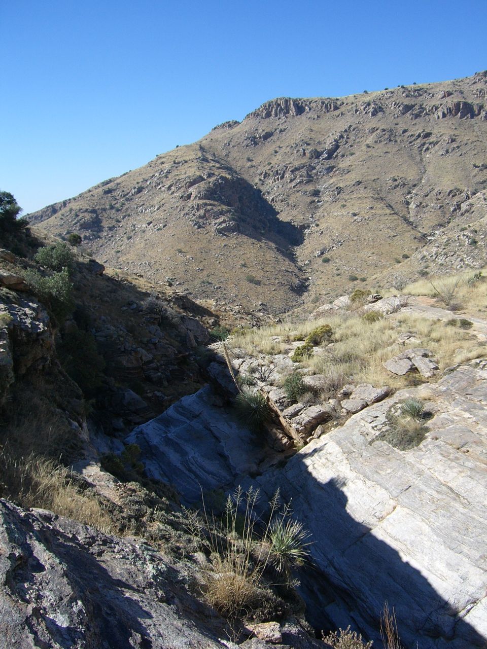 Mountain landscape with dry grass and rock formations under a clear blue sky