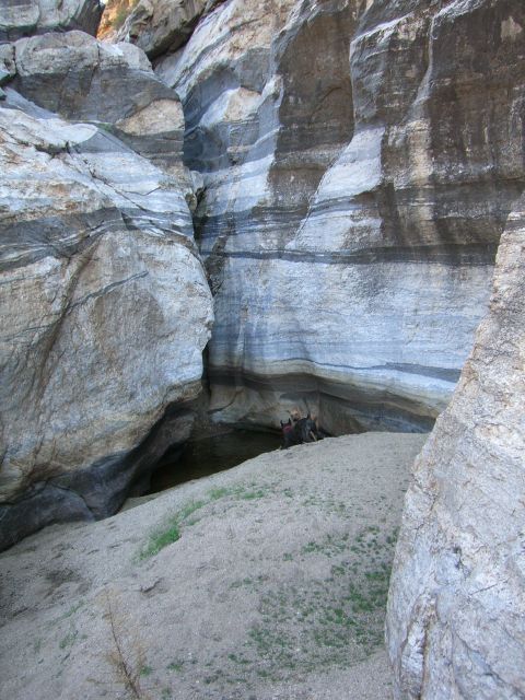 1996 Ford Probe - Layered rock formations create a dramatic scene within a canyon, with a small pool of water visible and two individuals exploring the area.