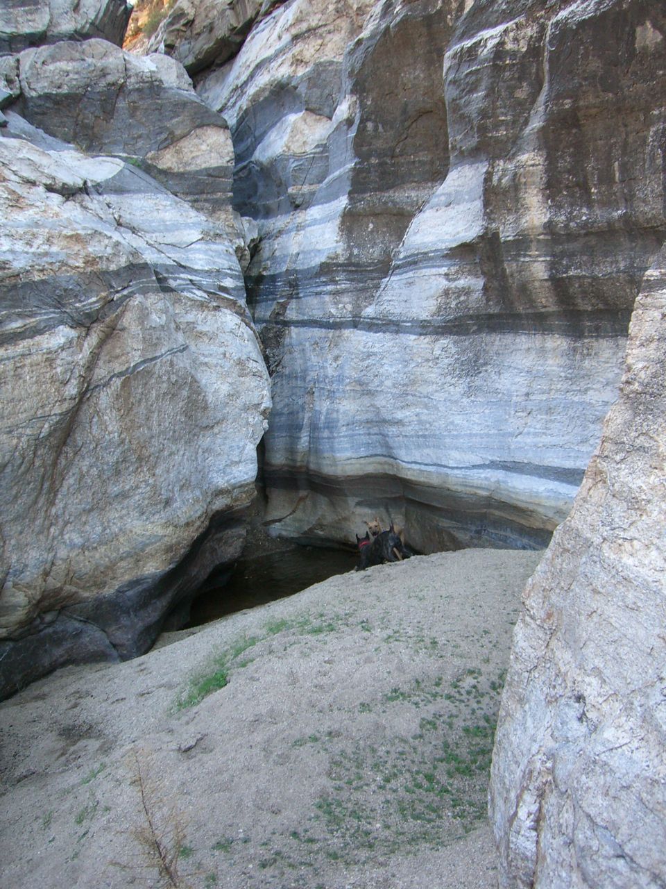 Layered rock formations in a canyon with a small pool of water and two people