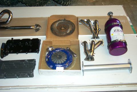 1996 Ford Probe - Various engine components, including exhaust headers, a clutch assembly, a flywheel, and a ZEX nitrous oxide bottle, are laid out on a surf…