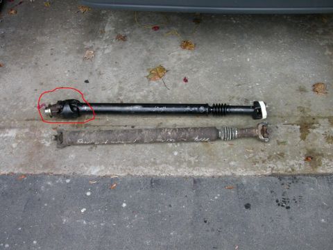 Two driveshafts on concrete, one black with a red circle around the U-joint, the other rusty with writing