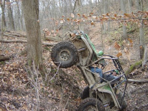 1992 Ford Bronco - Off-road buggy tipped on its side in woods with driver visible.