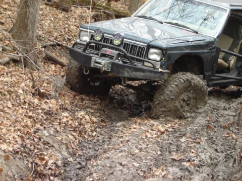 1992 Ford Bronco - This off-road vehicle is navigating a challenging muddy terrain with its front tires deep in the mire.