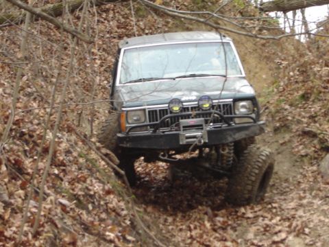 1992 Ford Bronco - A Jeep Cherokee XJ navigates a steep, wooded trail with muddy terrain.