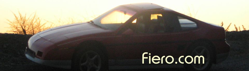 1986 Pontiac Fiero coupe with a white stripe on the hood, parked outdoors at sunset