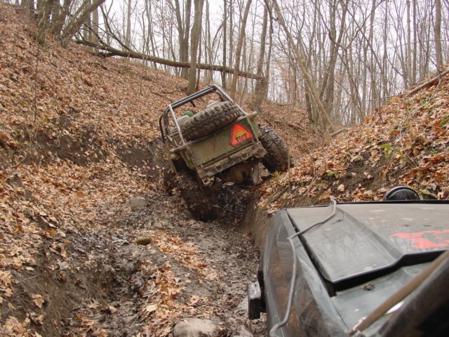 Two off-road vehicles navigating a muddy, leaf-strewn ditch in a wooded area
