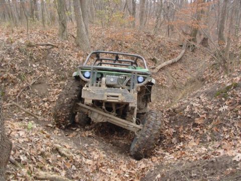 1992 Ford Bronco - An off-road vehicle tackles a challenging path through a forest with fallen leaves.