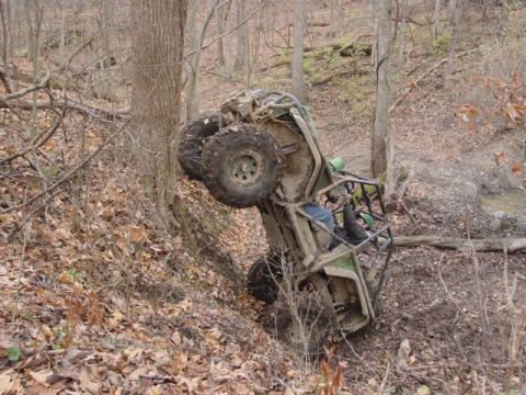 1992 Ford Bronco - An off-road vehicle has rolled onto its side in a muddy, wooded ravine.
