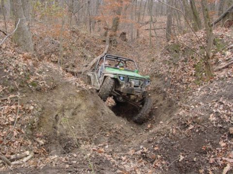 1992 Ford Bronco - An off-road vehicle navigates a steep, muddy trail in a forest.