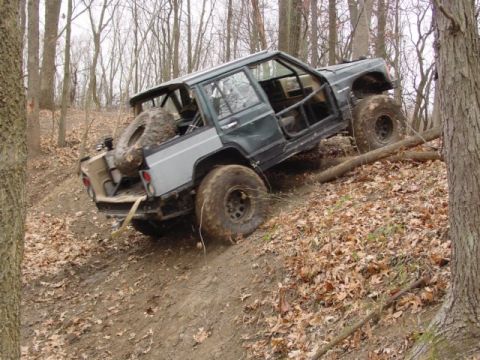 1992 Ford Bronco - Modified Jeep Cherokee XJ navigating a wooded off-road trail with large tires and a spare mounted in the rear.