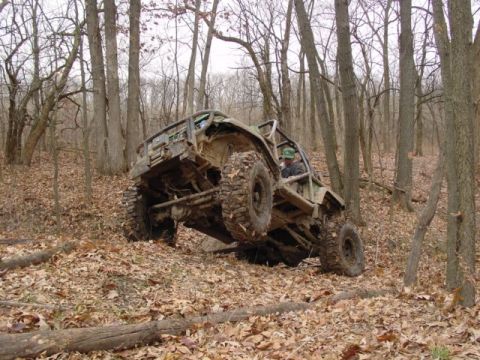 1992 Ford Bronco - A heavily modified off-road vehicle navigates a challenging trail in a forest environment.