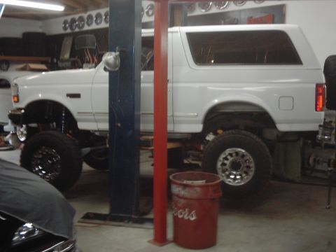 1978 Ford Bronco - Modified white Ford Bronco undergoing work in a garage, lifted on a hydraulic platform.