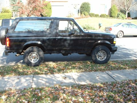 1994 Ford Bronco - This black 1994 Ford Bronco is seen from the side, parked on a sidewalk with fallen leaves.