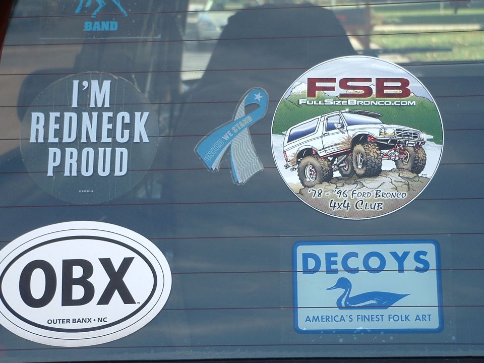 Vehicle window with 'I'm Redneck Proud' sticker, a blue ribbon sticker, an OBX sticker, a 'Decoys' sticker, and a circular sticker showing 'FSB FullSizeBronco.com '78-'96 Ford Bronco 4x4 Club'