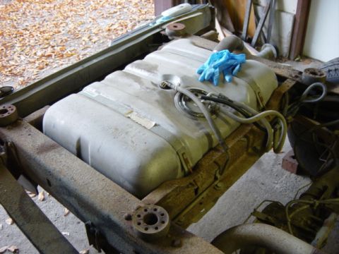 1991 Ford Bronco - A vehicle's fuel tank is shown installed on its frame, with fuel lines connected and a pair of blue gloves resting on top.