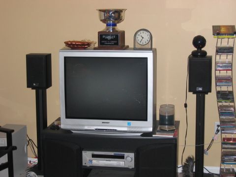 1985 Ford LTD Crown Victoria - A collection of electronics and awards are displayed on a stand against a wall.
