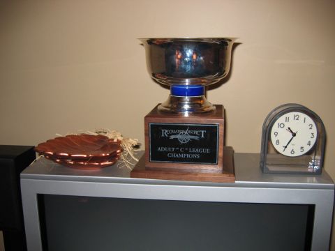 1985 Ford LTD Crown Victoria - A trophy and a clock sit on a shelf above a television, with a decorative wooden bowl to the left.
