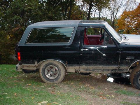1988 Ford Bronco - This black Ford Bronco is shown from the side, revealing its red interior and muddy lower body panels.