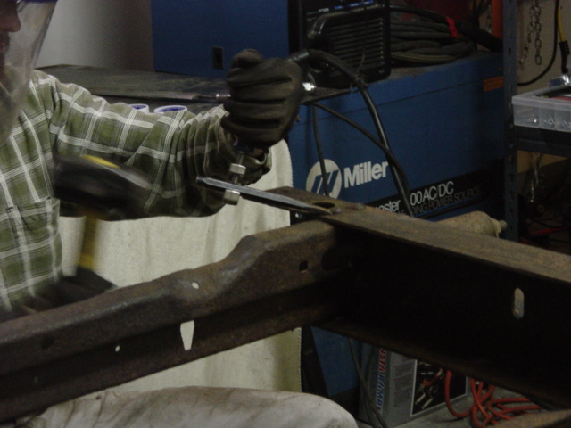 My aim's not really that bad, that's on the backswing.  My prescription for frame rivet removal -- undercut the head as much as you can with a 3" cutoff disk, and then break out the 5/8" cold chisel and (depending on the angle) the 24oz ball peen or the 4lb drilling hammer (shown).  

The little chisel holder I'm using was a Sears purchase yesterday (11/19), and was an extremely well spent $10 -- unless you have nerves of steel and either good aim or a steel wrist to match, there's no way you can put enough force on that chisel to do this job.  With the chisel holder and my hand out of the way, I could draw back a good two feet with the ball peen (or 18" with the hammer shown) and really beat the hell out of things.  After swinging that hammer for an hour your aim starts to suffer a little, and I'd have probably broken my wrist without the chisel holder.