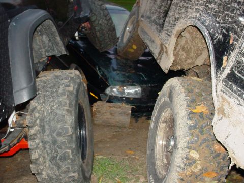 1988 Ford Bronco - Several heavily modified off-road vehicles are tightly packed together in a muddy environment.