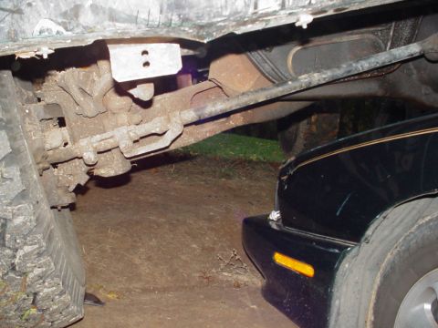 1988 Ford Bronco - Close-up view of a vehicle's undercarriage, with the fender of a black car visible on the right.
