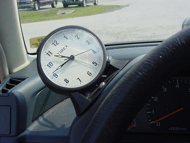 Dashboard clock with white face and black numbers, mounted on dashboard near steering wheel