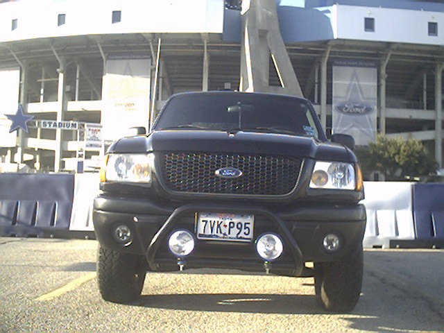 Black Ford Ranger pickup truck with bull bar and fog lights, front view, parked in front of a stadium