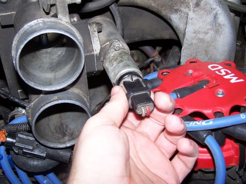 1986 Ford Bronco - Close-up of engine components, focusing on a sensor being disconnected from the throttle body assembly.
