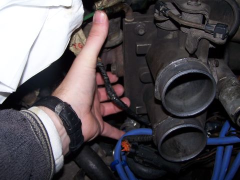 1986 Ford Bronco - Close-up of engine components, including a throttle body and intake manifold, with a hand present.
