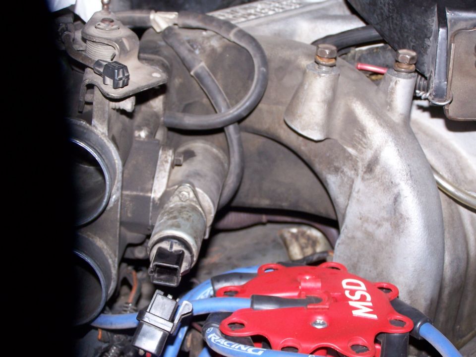 Idle air control valve on a cast intake plenum above a red MSD distributor cap and blue plug wires