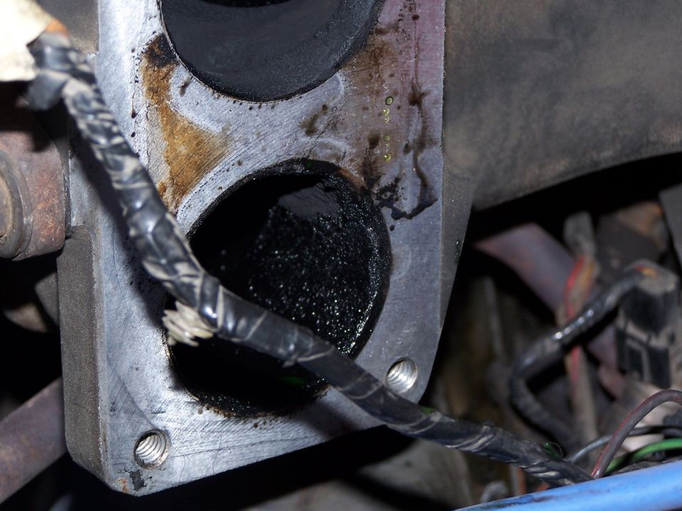 Carbon-caked twin-bore intake flange on an engine with taped wiring running across it