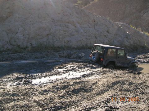 1985 Ford Bronco - A Jeep Wrangler is stuck in thick mud, with its rear tire showing.
