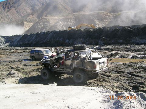 1985 Ford Bronco - Two off-road vehicles are stuck in a muddy, mountainous terrain with construction equipment visible in the distance.