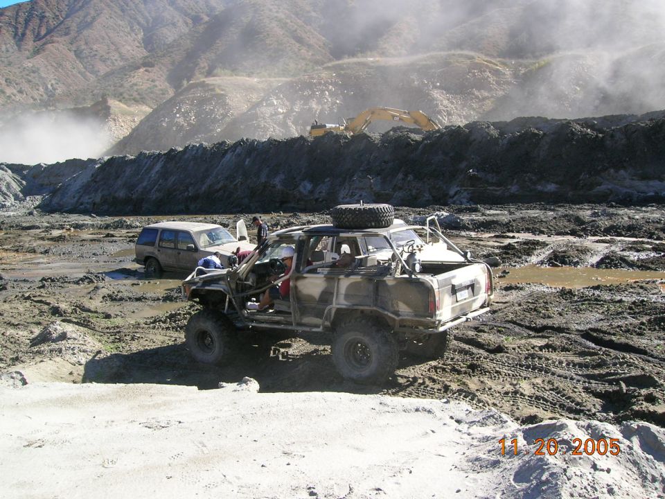 Modified off-road SUV and another SUV stuck in mud with construction equipment in background