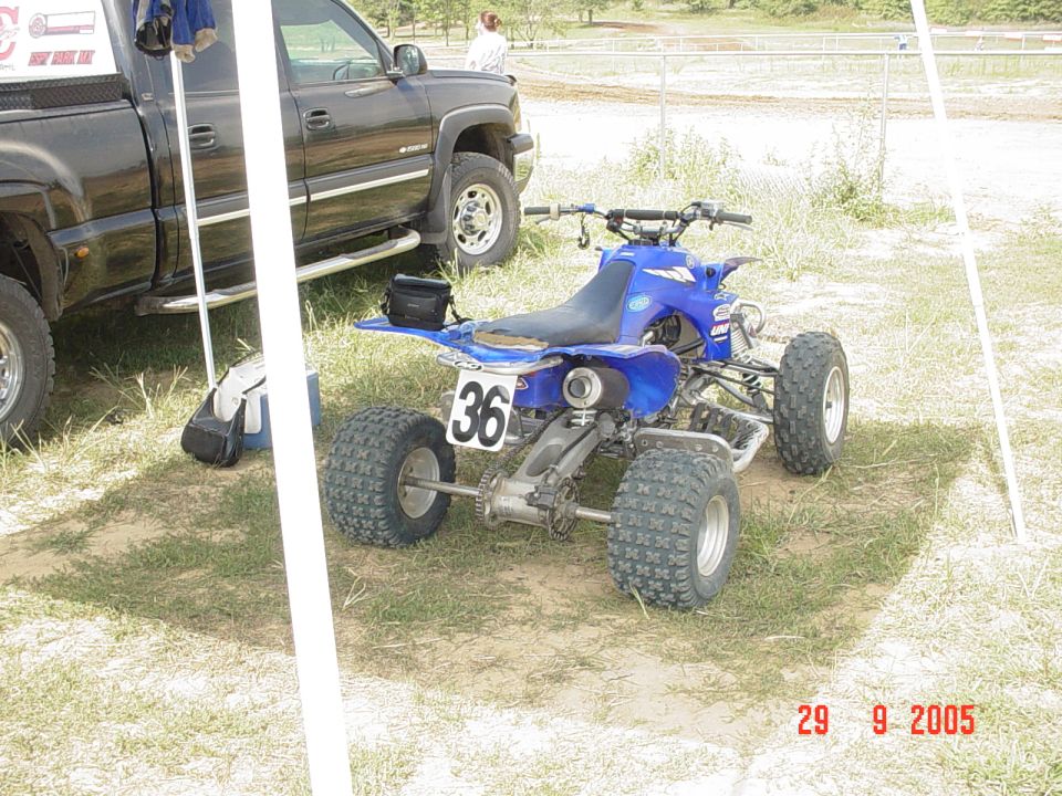 Blue Yamaha sport quad ATV with number 36 parked by a black pickup on grass