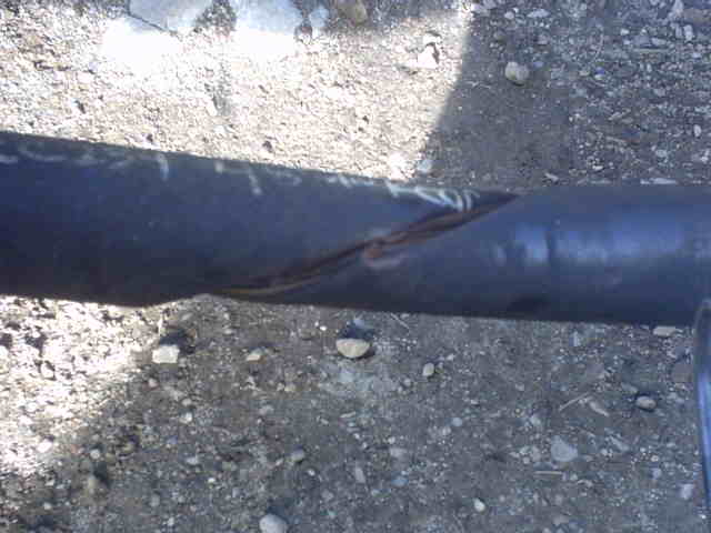 Black steel tube axle housing twisted and kinked, lying on gravel