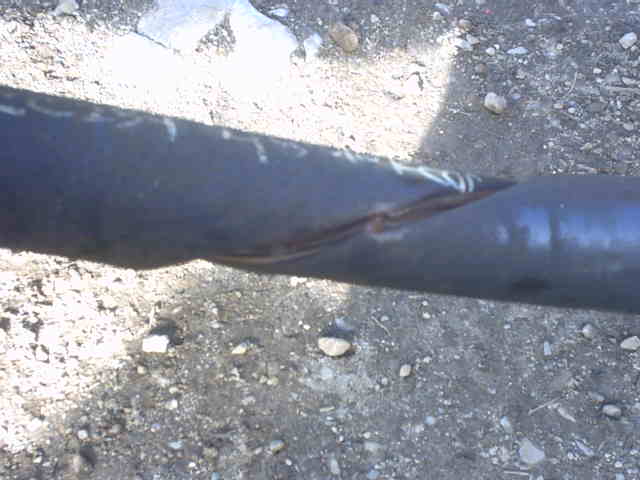 Close-up of a bent and creased black steel tube with rust in the fold