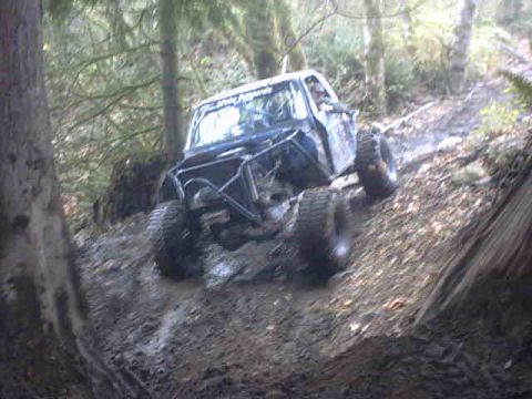 1995 Ford Bronco - Off-road Bronco navigates a challenging muddy incline in a forest setting.