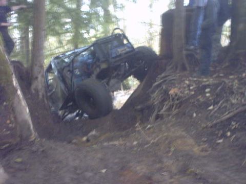 1995 Ford Bronco - An off-road vehicle is stuck on its side in a muddy, wooded area.