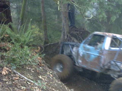 1995 Ford Bronco - This heavily modified truck navigates a challenging muddy trail in a wooded area.