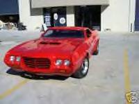 1972 Ford Ranchero - A bright red 1972 Ford Ranchero is parked outside a building, showing its distinctive front end and coupe utility body style.