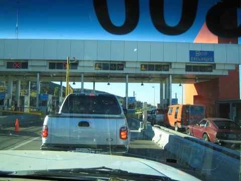 1990 Ford Bronco - Through a windshield, a silver pickup and other vehicles queue at a multi-lane border or toll crossing marked Exclusivo.