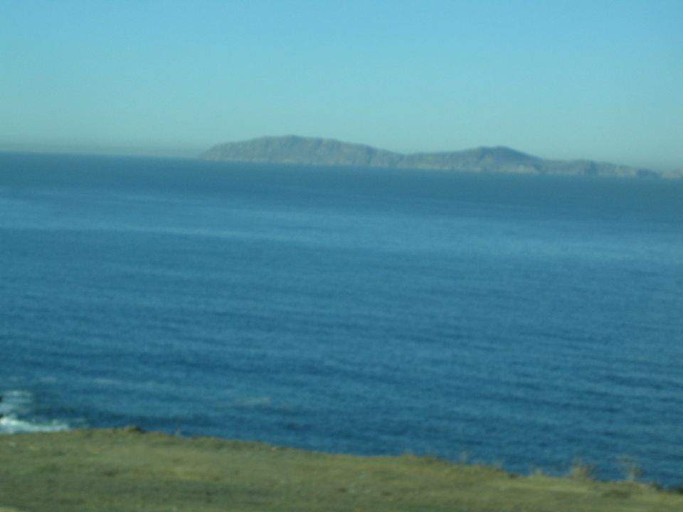 Distant island or headland across calm blue ocean seen from a grassy bluff